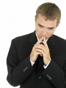 Man in black suit in a thinking pose with hands clasped close to face